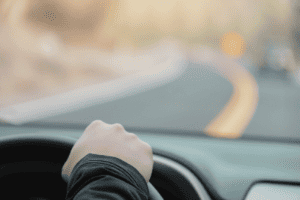 Hand on a steering wheel in a car with a background image of the road ahead.